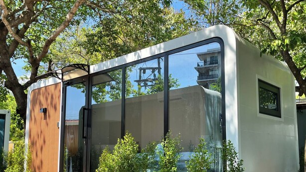 Una autocaravana moderna y compacta con un amplio ventanal, terraza de madera y un pequeño jardín.