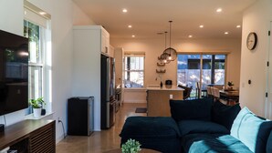 Una sala de estar moderna con un televisor grande, una mesa de centro de madera y un sofá verde oscuro.