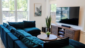 Una sala de estar moderna con un sofá modular, un televisor de pantalla plana, una mesa de centro de madera y una planta en maceta.