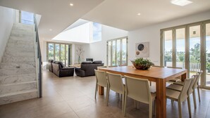 A spacious living area with a wooden dining table, white chairs, a staircase, and a large window offering a view of the outdoors. - Unique villa with swimming pool located in the mountains (Las Palmeras)