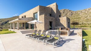 A modern house with a stone facade, a covered patio with lounge chairs, and a view of the surrounding hills. - Unique villa with swimming pool located in the mountains (Las Palmeras)
