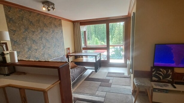 A spacious living room with a large window, a wooden coffee table, a sofa, and a television. - Les arcs 1800 - T2 827 - 5 pers parking/housekeeping included (Bourg-Saint-Maurice)
