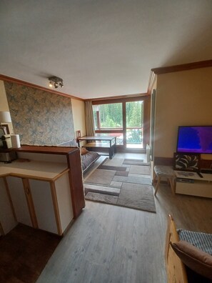 A spacious living room with a large window, a wooden coffee table, a sofa, and a television. - Les Arcs 1800 - T2 827 - 5 people Parking/Cleaning Included (Bourg-Saint-Maurice)