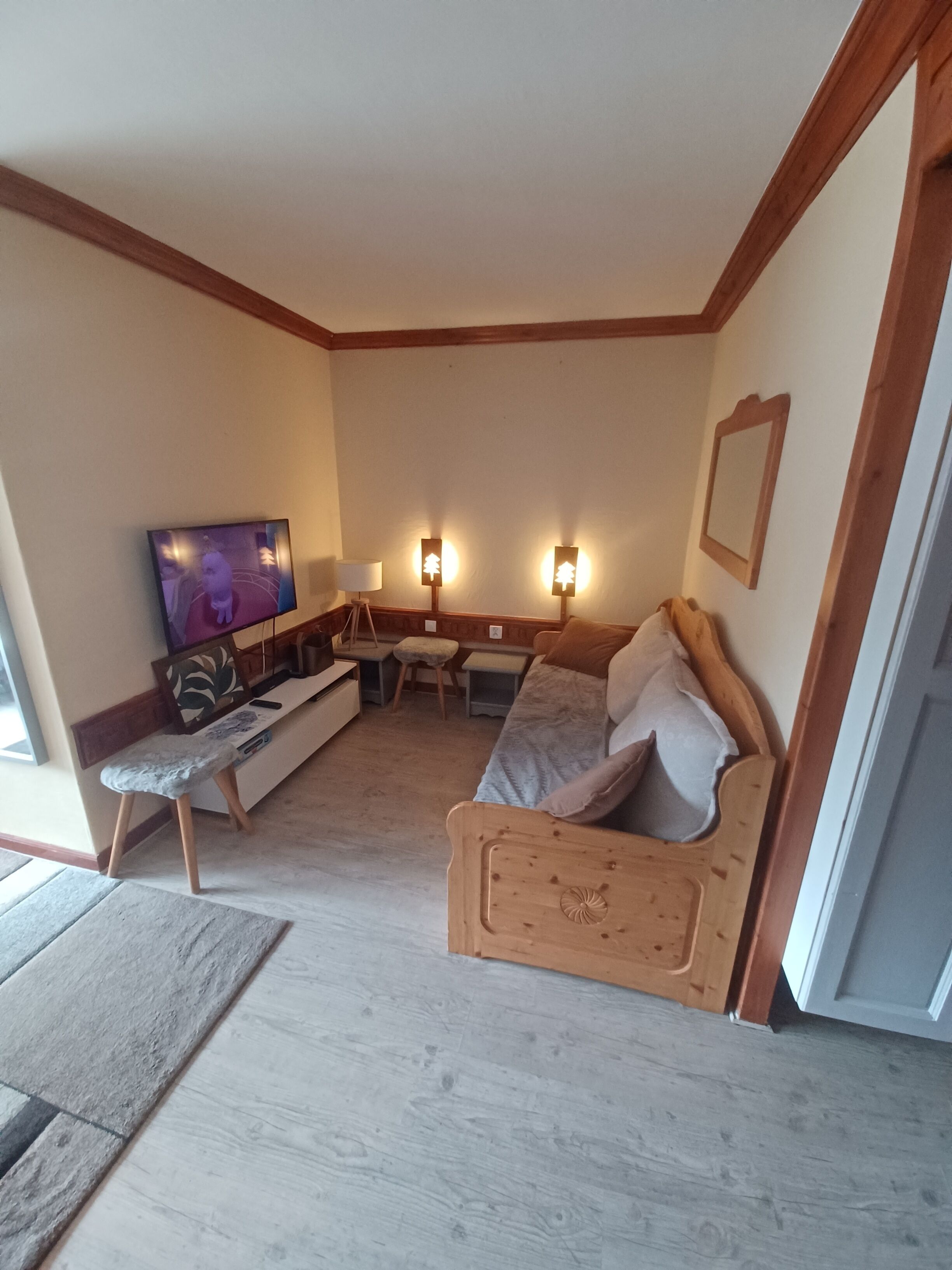 A cozy living room with a wooden sofa, a television, a small table, and two wall-mounted lamps.