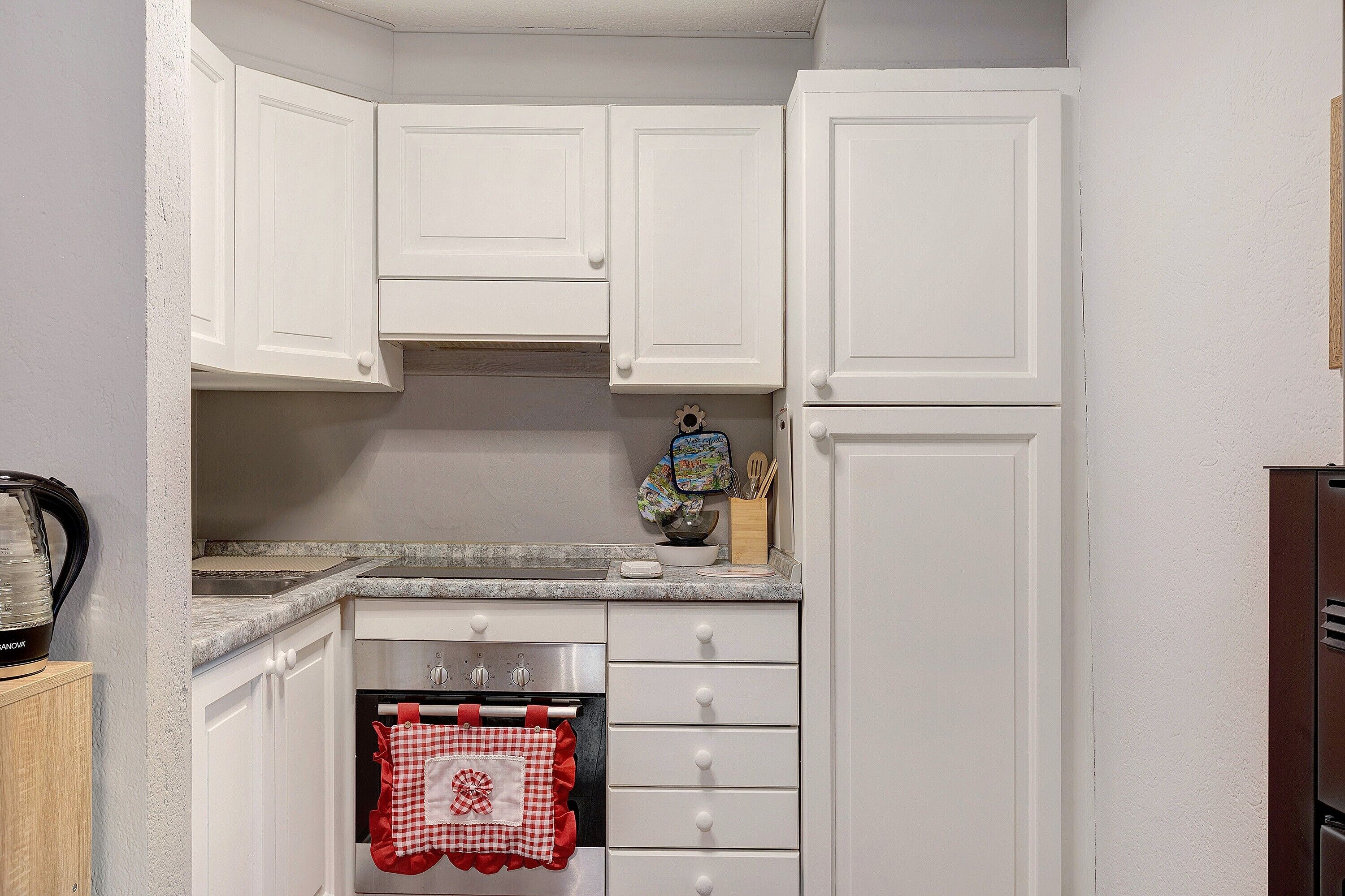A compact kitchen with white cabinets, a built-in oven, and a countertop with a coffee maker.