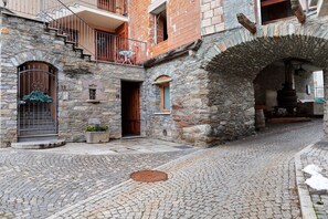 A cobblestone street with a stone building featuring a staircase, a door, and a window.