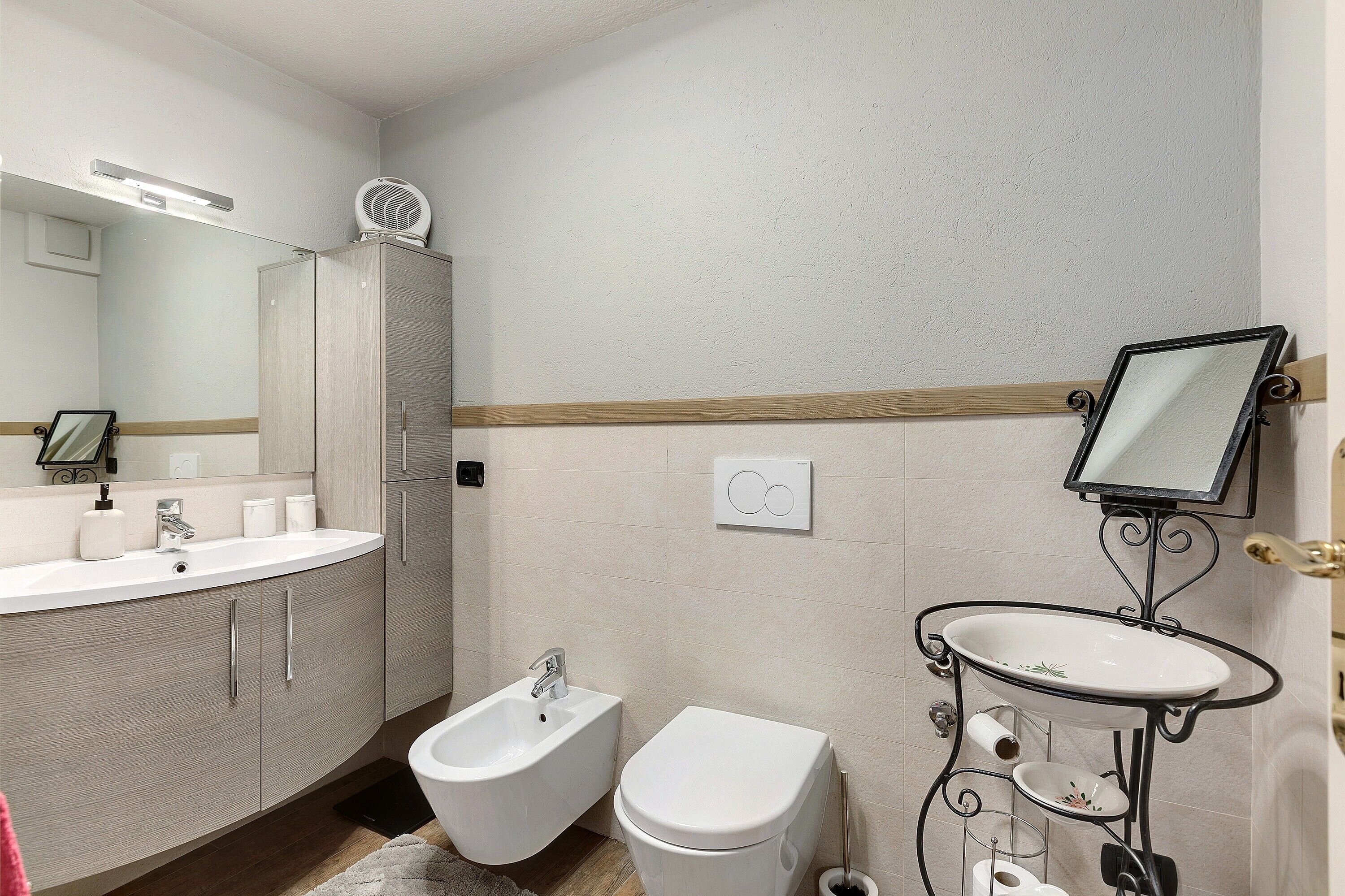 Een badkamer met een bidet, een wastafel, een spiegel en een kast.