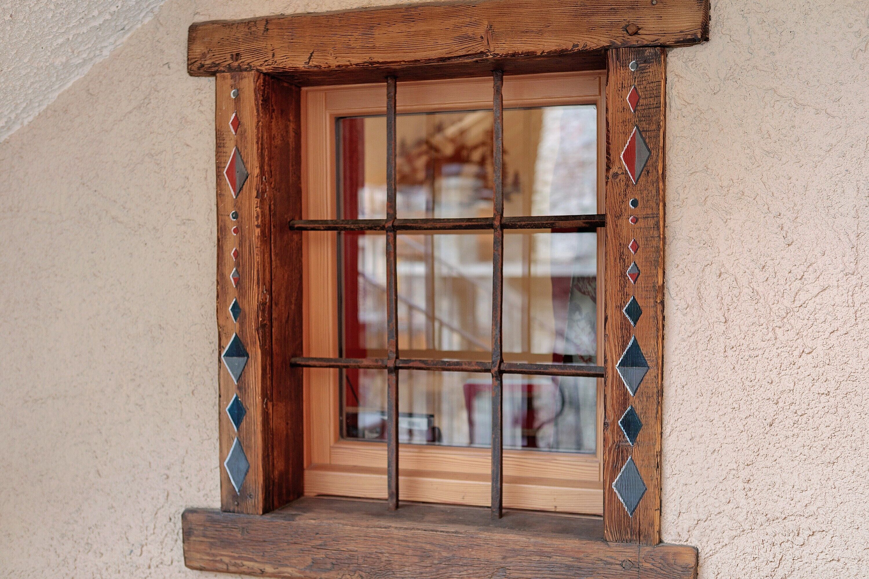 Una ventana con marco de madera y barrotes de metal, en una pared con textura.