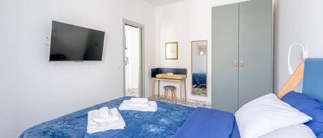 A modern hotel room with a large bed, a desk, a wardrobe, and a flat-screen TV.
