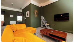 Una sala de estar moderna con un sofá amarillo, una mesa de centro de madera, un televisor montado en la pared y un espejo decorativo con forma de sol.