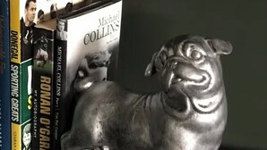 Una estatua metálica de un león sobre una estantería con libros, entre ellos títulos como