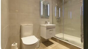 Un baño moderno con inodoro, lavamanos y ducha envuelta en vidrio.