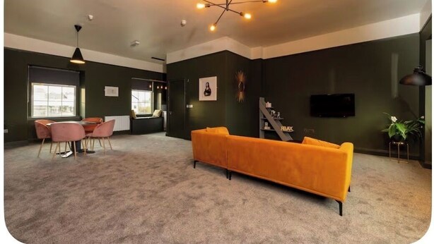 Un espacio habitable amplio con un sofá naranja grande, una mesa de comedor con sillas rosadas y una lámpara de araña moderna.