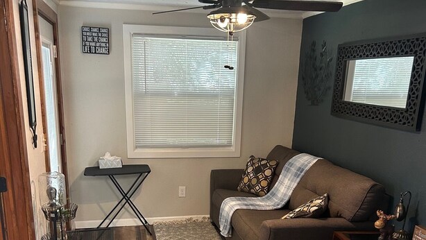 A cozy living room with a brown couch, a small table, a ceiling fan, and a window with blinds. - Adorable 1-bedroom bungalow with AC in Sergeant Bluff (Sergeant Bluff)