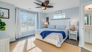 Ein Schlafzimmer mit einem Bett, zwei Nachttischen, einem Deckenventilator, einem Fenster mit Vorhängen und einem an der Wand befestigten Schild.