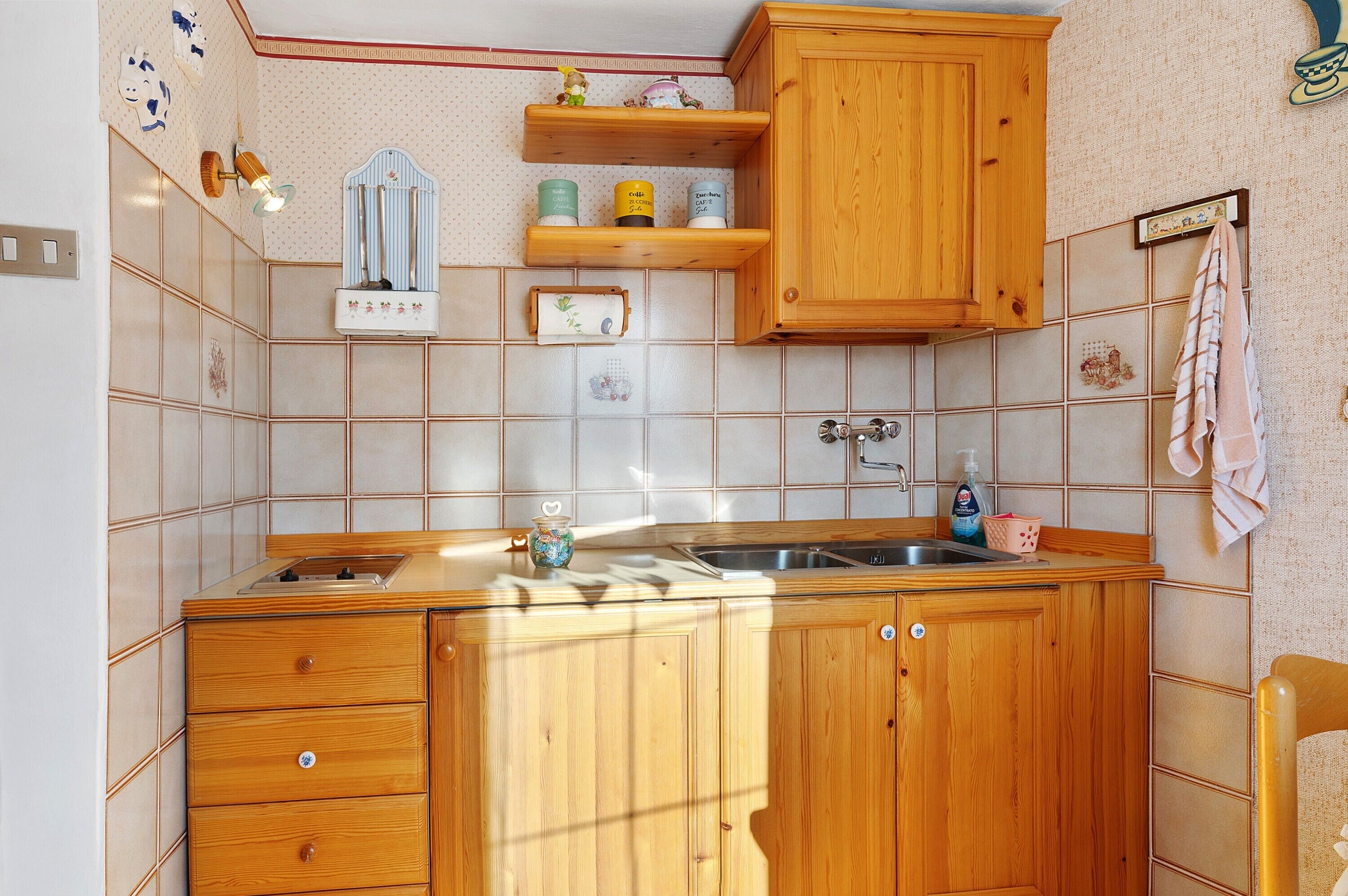 A kitchen with wooden cabinets, a sink, and a countertop. There are shelves above the sink with decorative items.