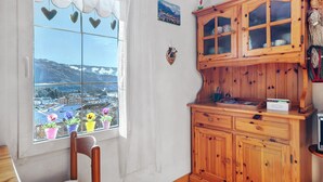 A kitchen with wooden cabinets, a window with a view of a town and mountains, and a chair. - Casa Zarina, charming two-room apartment in Cavalese (Cavalese)