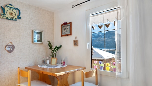 A wooden dining table with chairs, a window with heart-shaped decorations, and a view of mountains. - Casa Zarina, charming two-room apartment in Cavalese (Cavalese)