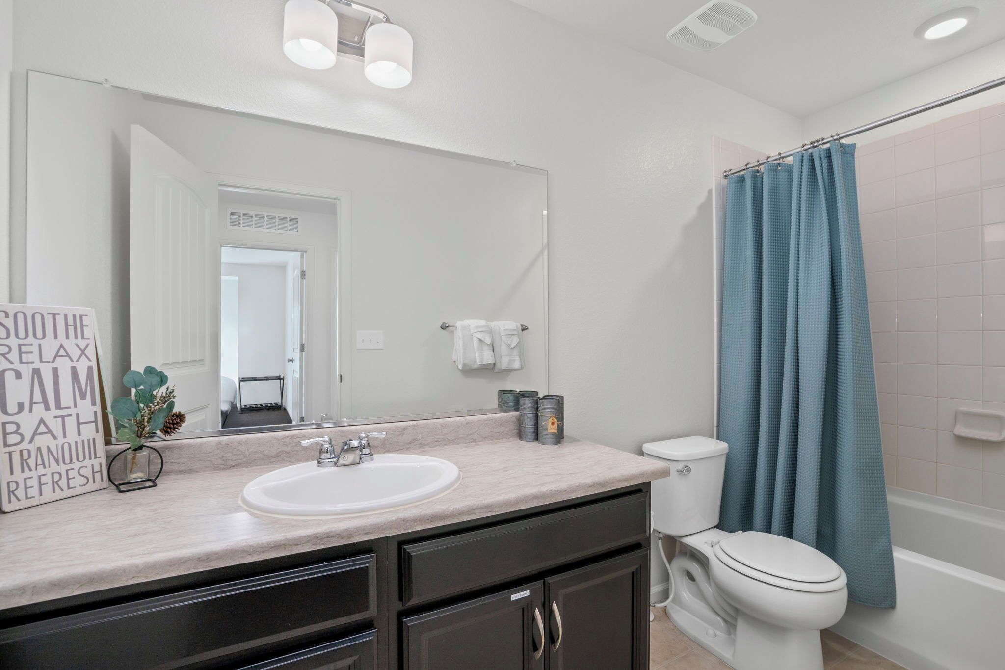 A bathroom with a white sink, dark cabinets, a toilet, and a blue shower curtain.