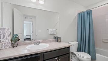 A bathroom with a white sink, dark cabinets, a toilet, and a blue shower curtain.
