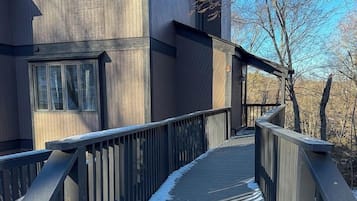 Una terraza de madera que conduce a un edificio moderno con ventanas grandes y una chimenea.