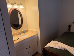 Ein Badezimmer mit einem runden Spiegel, einem Waschbecken und einem Bett mit einer grünen Matratze und weißer Decke.