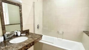 Ein Badezimmer mit Marmorwaschbecken, Spiegel, Badewanne und gefliesten Wänden.