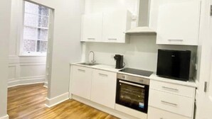 Eine kleine Küche mit weißen Schränken, einem eingebauten Backofen, einer Kaffeemaschine und einem schwarzen Kühlschrank.