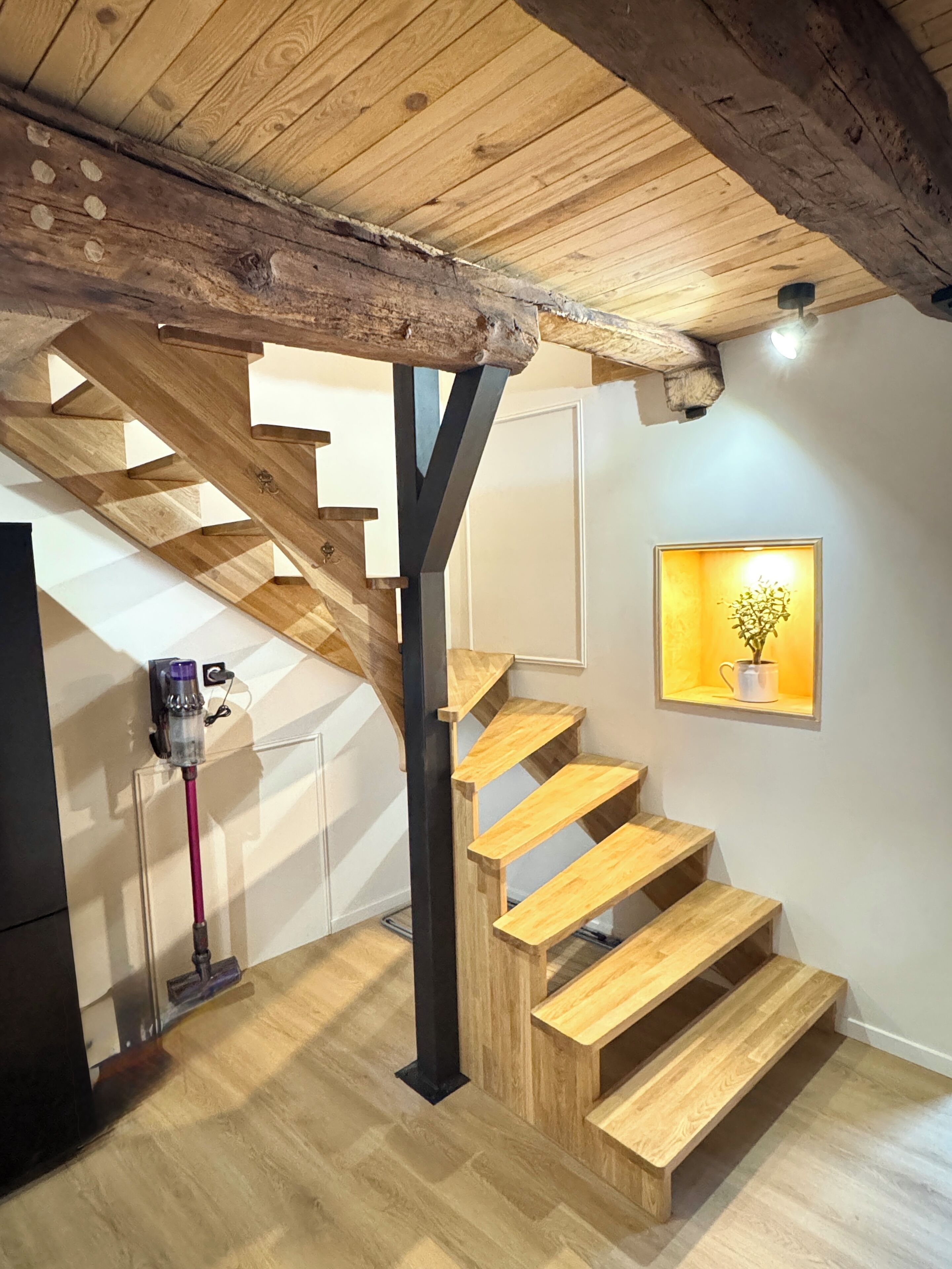 A wooden staircase with a modern design, a wall-mounted light fixture, and a framed picture of a plant.