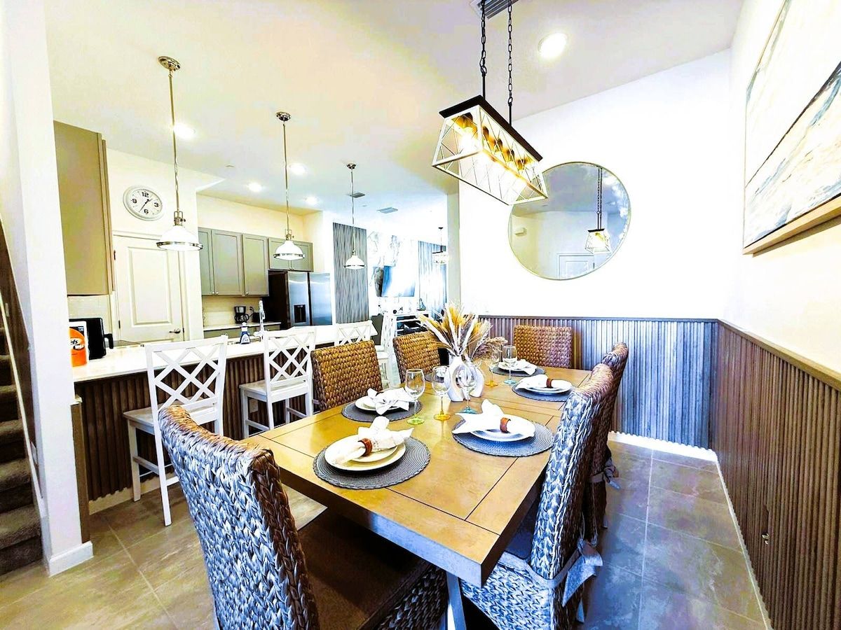 A dining area with a wooden table set for six, surrounded by upholstered chairs.