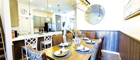 A dining area with a wooden table set for six, surrounded by upholstered chairs.