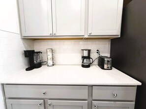 Una cocina con armarios blancos, una cafetera, un tostador y una licuadora sobre la encimera.