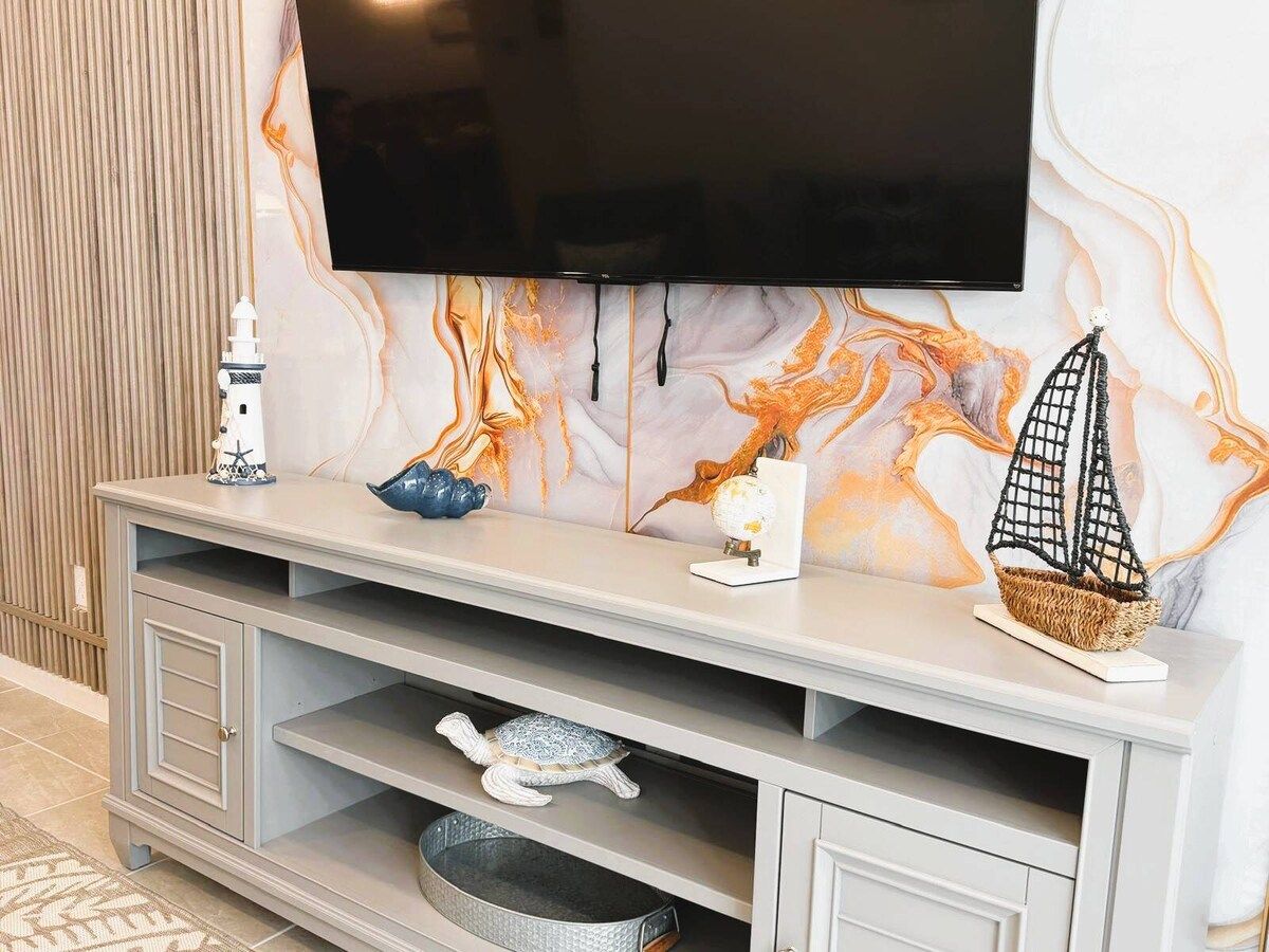 Un moderno salón con un televisor de pantalla plana montado en una pared de mármol, una consola decorativa y una estantería empotrada.