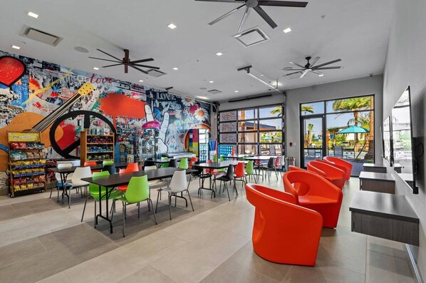 Una cafetería moderna con sillas de colores, un mural y vistas al exterior.