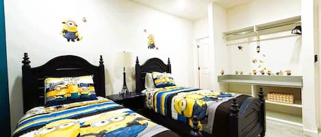 Ein Schlafzimmer mit zwei Betten, beide mit Minion-Motiv. Eine weiße Wand ist mit Minion-Aufklebern versehen, ebenso eine weiße Tür und ein weißes Regal.