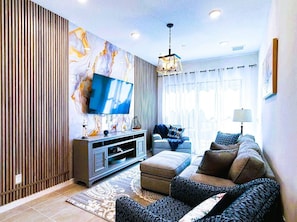 A modern living room with a flat-screen TV, a sofa set, a coffee table, and a decorative wall with a marble-like pattern. - 10466 Upscale Paradiso Townhome: Private Pool (Orlando)