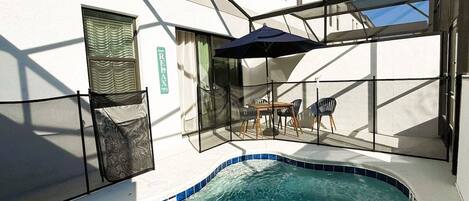 A swimming pool with a glass enclosure, a table with chairs, and a door with a window.