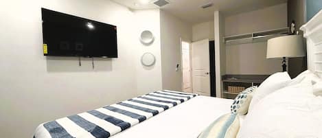 Een slaapkamer met een bed, een aan de muur bevestigde televisie, een deur en een nachtkastje met een lamp.