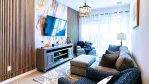 Un salon moderne avec un téléviseur à écran plat, un canapé, un tapis à motifs et un mur décoratif.