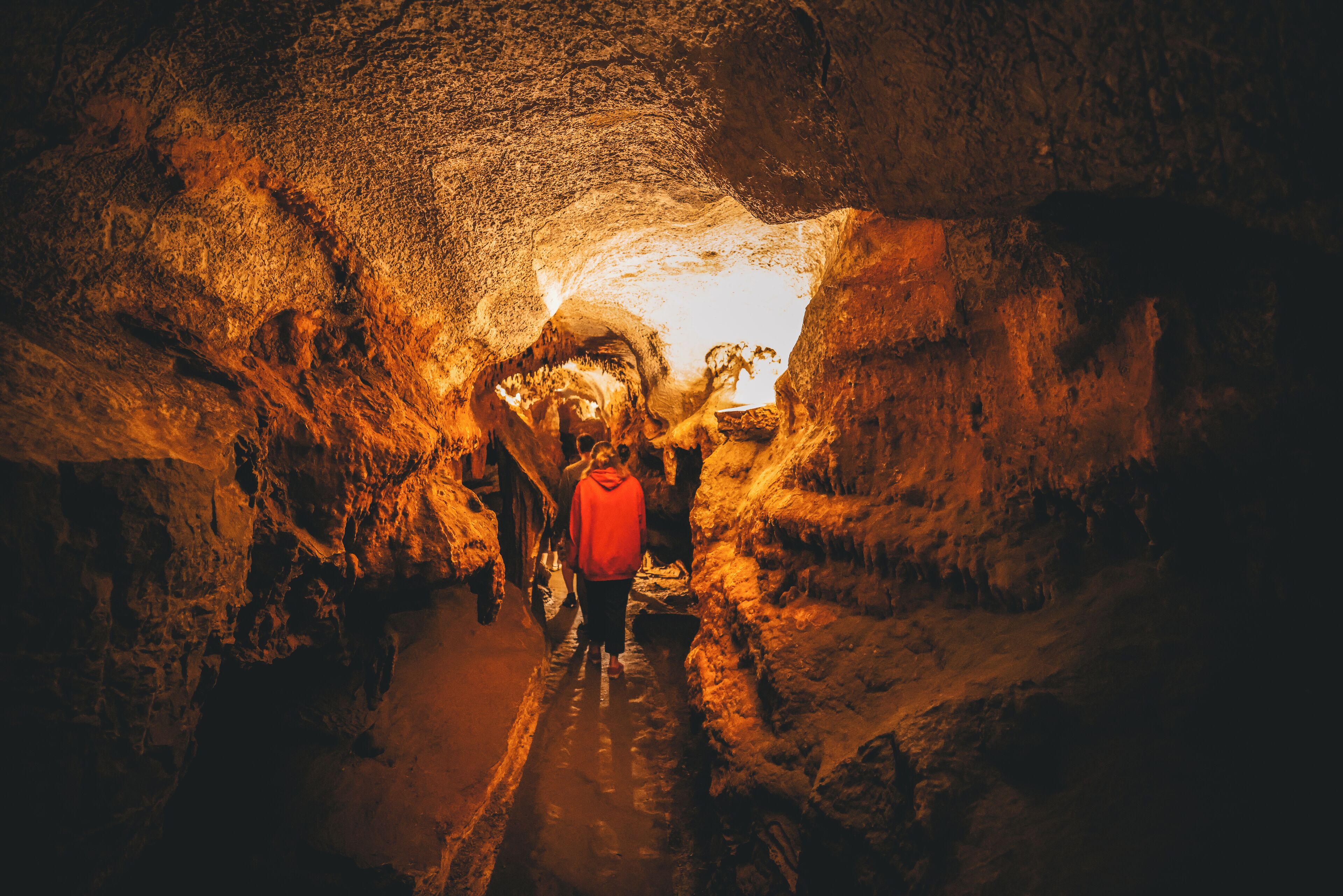 A person walking through a narrow, rocky tunnel with a warm light source at the end.
