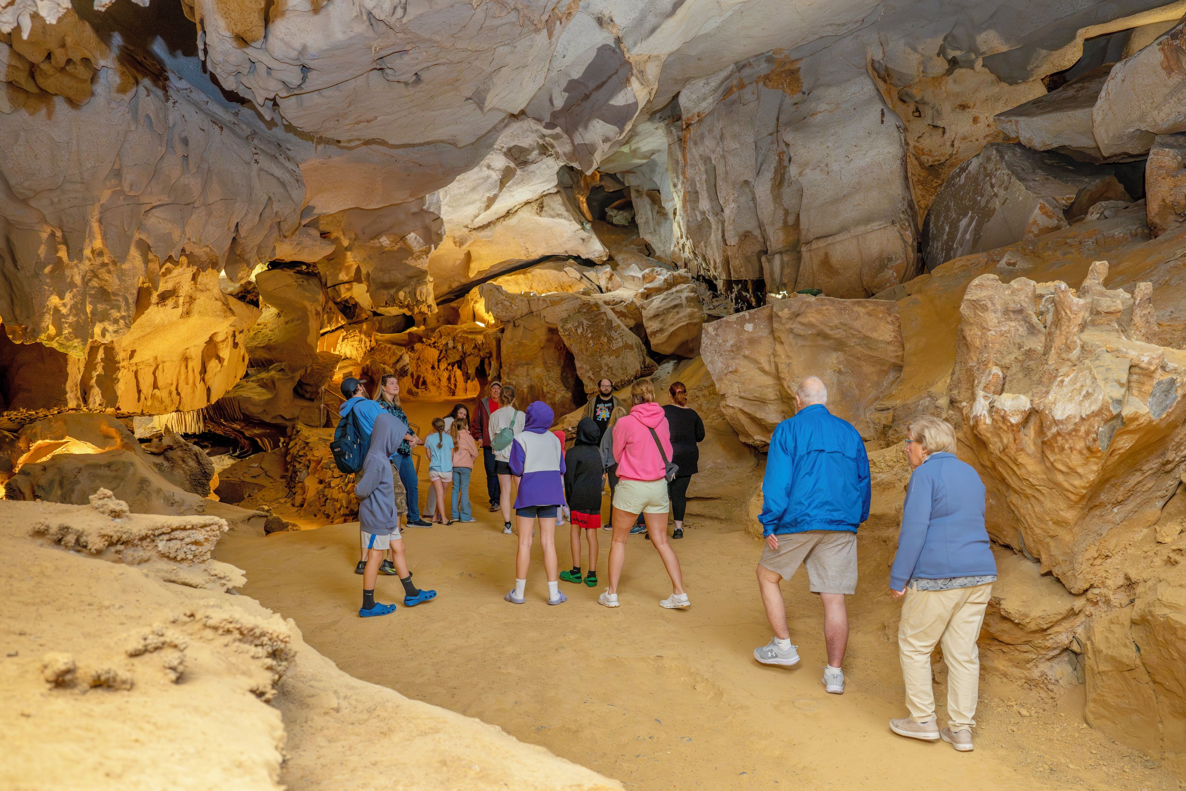 Un groupe de personnes se trouve à l’intérieur d’une grotte, où l’on peut observer des formations rocheuses et un sol sablonneux.