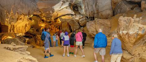 A group of people inside a cave with rock formations and a sandy floor.