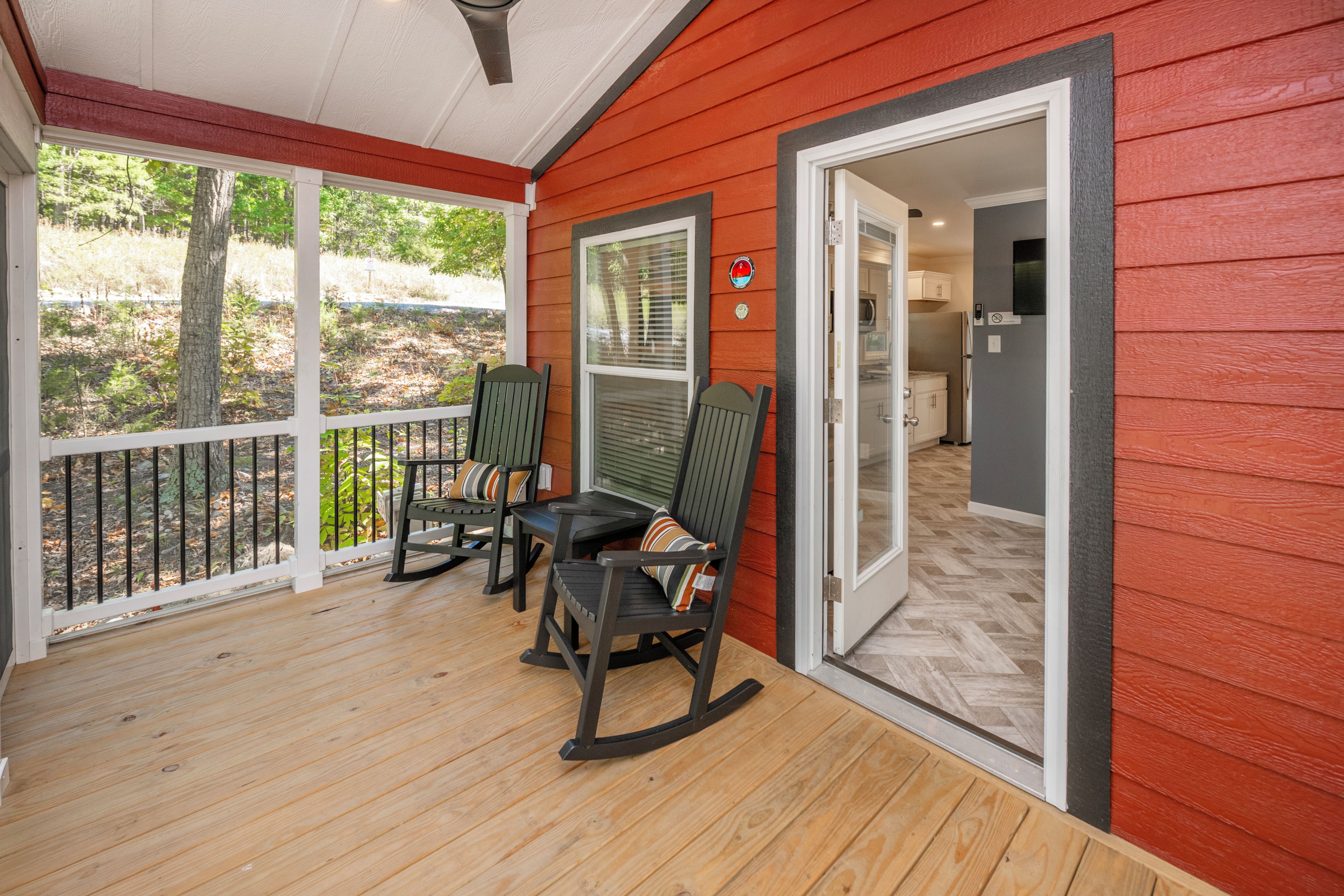 A covered porch with wooden flooring, two rocking chairs, and a door leading to a kitchen area.
