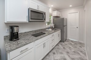 A modern kitchen with white cabinets, a granite countertop, a built-in microwave, a coffee maker, a stainless steel refrigerator, and a herringbone-patterned floor. - Endless Caverns RV Resort & Cavern Tours (New Market)