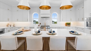 A modern kitchen with white cabinetry, a central island, pendant lighting, and a view through the windows. - Casamigos: Stunning Sugar Sands home w/ Private Pool, Sleeps 16, Pet-Friendly (Mecixo Beach)