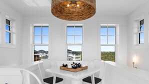 A white interior with a dining table, chairs, and a wicker ceiling light fixture. - Casamigos: Stunning Sugar Sands home w/ Private Pool, Sleeps 16, Pet-Friendly (Mecixo Beach)