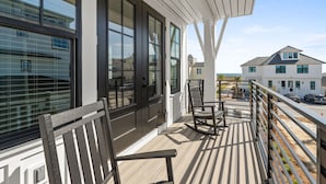 A balcony with wooden flooring, a rocking chair, and a table. - Casamigos: Stunning Sugar Sands home w/ Private Pool, Sleeps 16, Pet-Friendly (Mecixo Beach)