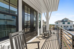 A balcony with wooden flooring, a rocking chair, and a table. - Casamigos: Stunning Sugar Sands home w/ Private Pool, Sleeps 16, Pet-Friendly (Mecixo Beach)
