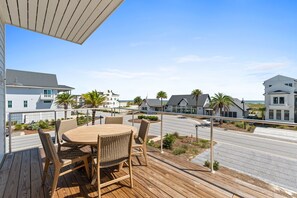 A wooden deck with a round table and chairs, overlooking a street with houses and a clear sky. - Gulfstone: Gulf Front New Build, Private Pool, Pet Friendly, Sugar Sands Communi (Mexico Beach)