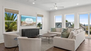 Een ruime woonkamer met een grote flatscreen-tv, comfortabele zithoek en uitzicht op het strand.